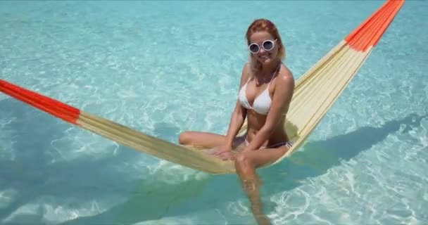 Mujer alegre sentada en la hamaca sobre la piscina — Vídeos de Stock