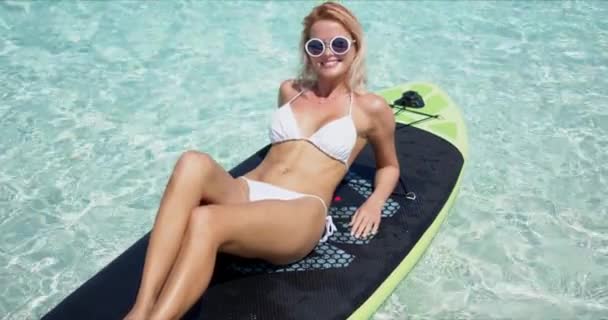 幸せなブロンド女性日光浴オンパドルボード — ストック動画
