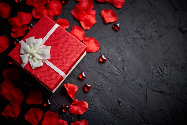 Caja de regalo sobre mesa de piedra negra. Fondo romántico de vacaciones con pétalos de rosa — Foto de Stock