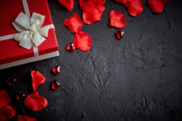 Caja de regalo sobre mesa de piedra negra. Fondo romántico de vacaciones con pétalos de rosa — Foto de Stock