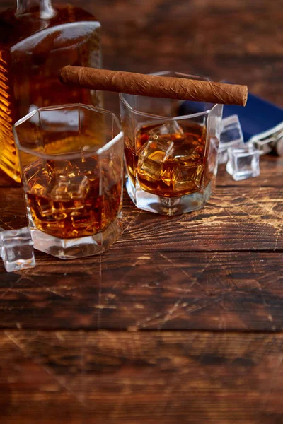 Botella de whisky con dos vasos y cigarro cubano colocado sobre mesa de madera rústica — Foto de Stock