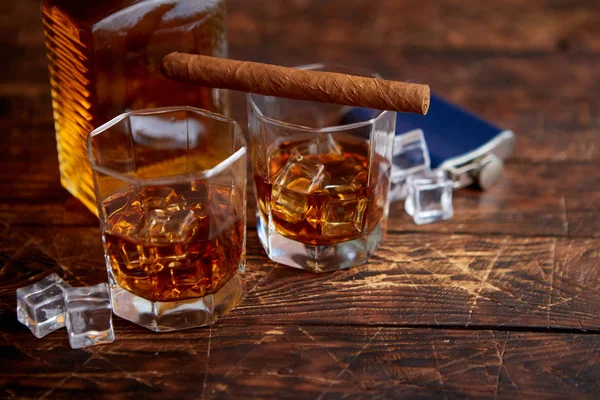 Botella de whisky con dos vasos y cigarro cubano colocado sobre mesa de madera rústica — Foto de Stock