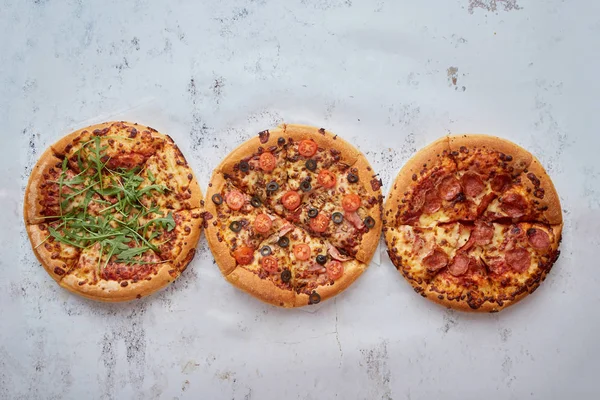 Trzy różne rodzaje pizzy umieszczone w rzędzie na białym zardzewiałym stole — Zdjęcie stockowe