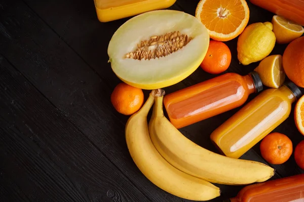 Fruits jaunes et orange et jus en bouteille placés sur un fond en bois noir — Photo