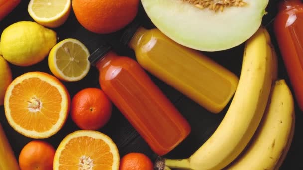 Жовті та апельсинові фрукти та пляшкові соки, розміщені на чорному дерев'яному фоні — стокове відео