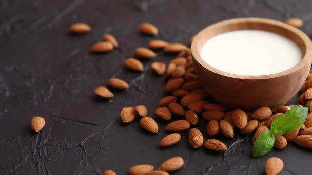 Latte di mandorla fresco in ciotola di legno e mandorle su fondo di pietra nera — Video Stock