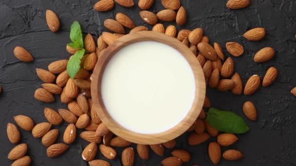 Fresh almond milk in wooden bowl and almonds on black stone background — Stock Video