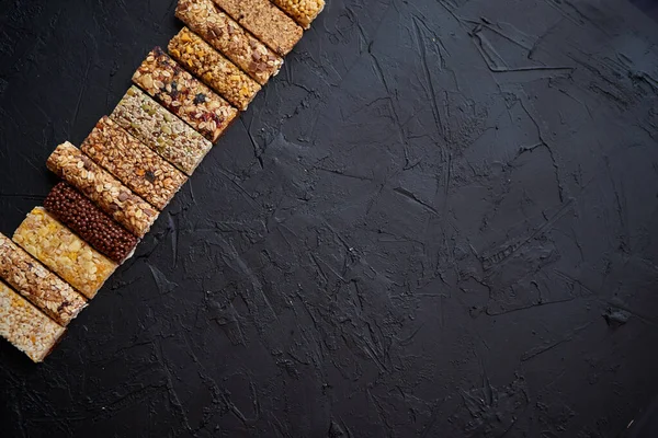 Diverses barres de granola saines placées en rangée sur une table en pierre noire — Photo