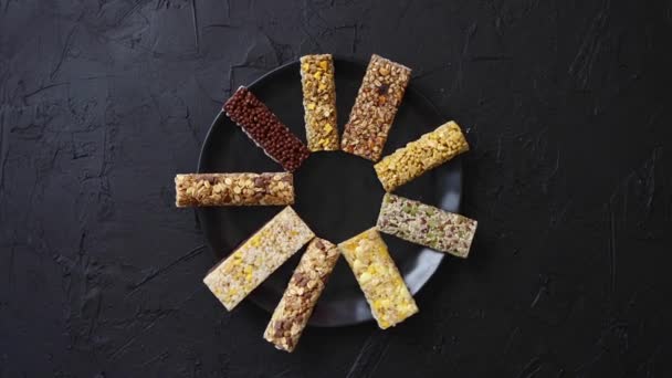 Diferentes tipos de barras de granola colocadas en una mesa sobre una placa de cerámica negra — Vídeo de stock
