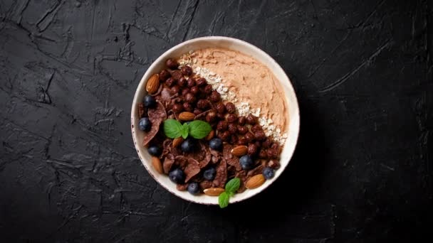 Chocolade en bosbessen smoothie of yoghurt. met cacaocornflakes, granola, muntblaadjes en amandelen — Stockvideo