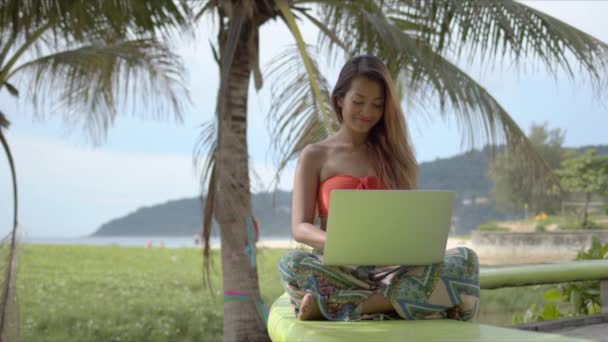 Красивая смешанная раса девушка сидит скрестив ноги и просматривает ноутбук — стоковое видео