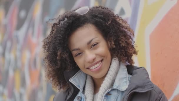 Mulher jovem sorridente bonita com corte de cabelo afro posando ao ar livre com graffiti — Vídeo de Stock