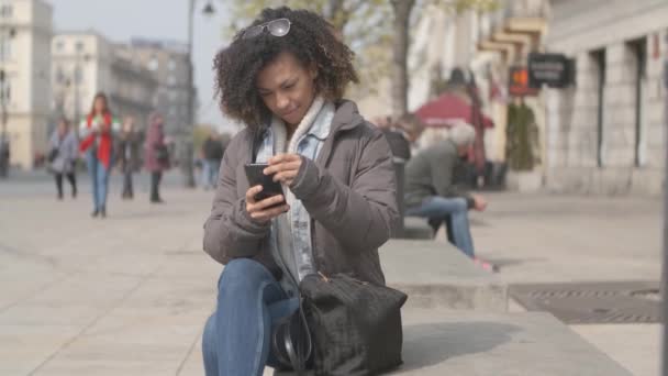 Hermosa chica con corte de pelo afro sentado en el banco en la calle de la ciudad — Vídeo de stock