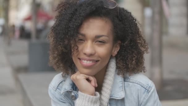 Vacker flicka med afro frisyr sitter på bänken på stads gatan — Stockvideo