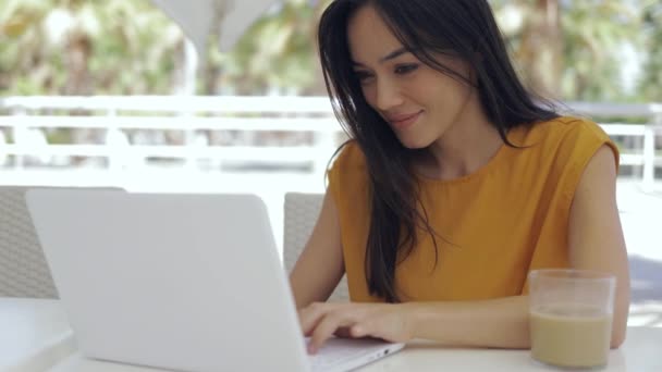 Adorable mujer de raza mixta sentada en la mesa de la cafetería al aire libre y usando computadora portátil — Vídeos de Stock