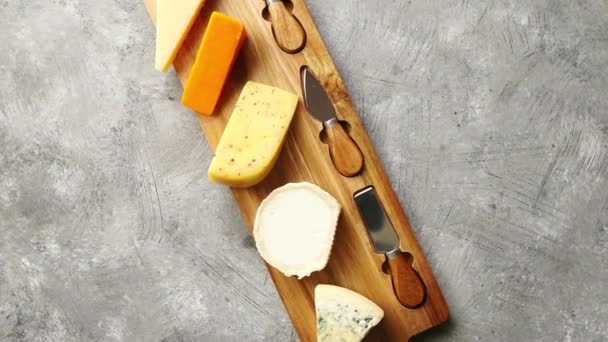 Асортимент різних видів сирів, що подаються на дерев'яній дошці з виделкою та ножами — стокове відео