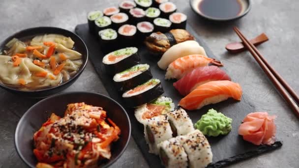 Složení různých druhů sushi válců umístěných na černé kamenné desce — Stock video