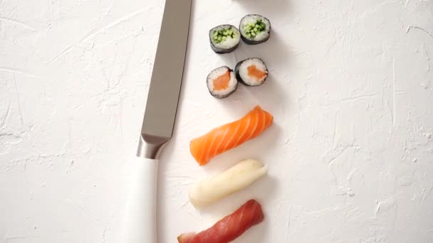 Różne sushi rolki z japońskim nożem na białym kamiennym tle łupka — Wideo stockowe
