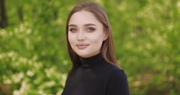 Porträtt av ung kvinna i svart skjorta och med långt hår tittar på kameran — Stockvideo