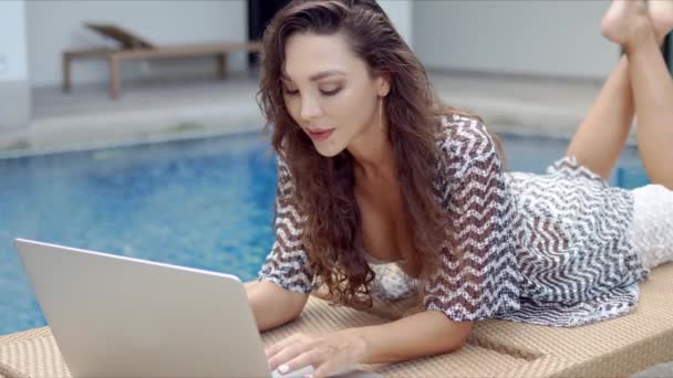 Стильная женщина с ноутбуком, отдыхающая у бассейна — стоковое видео