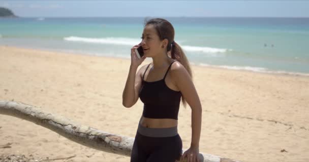 Vrolijke etnische sportvrouw spreekt op smartphone op het strand — Stockvideo