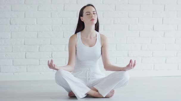 Genç bir kadın beyaz odada meditasyon yapıyor. — Stok video