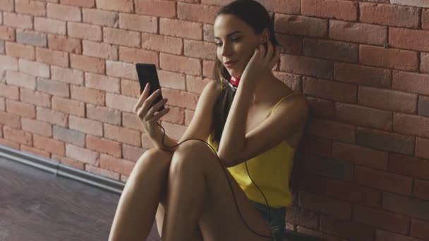Aantrekkelijke jonge vrouw met moderne koptelefoon browsen smartphone en luisteren naar de muziek — Stockvideo
