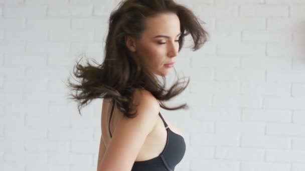 Atractiva joven hembra en sujetador negro tocando el pelo y mirando a la cámara — Vídeo de stock