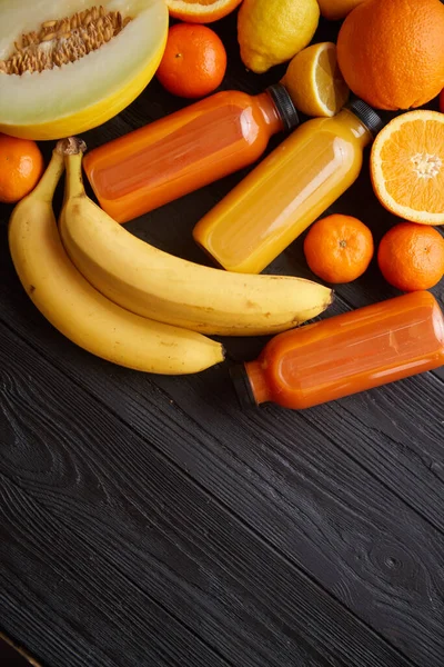 Frutas amarillas y anaranjadas y jugos embotellados colocados sobre fondo de madera negro —  Fotos de Stock