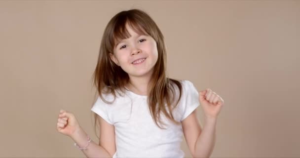 Милая маленькая девочка в белой футболке танцует, улыбается и веселится в студии сессии — стоковое видео
