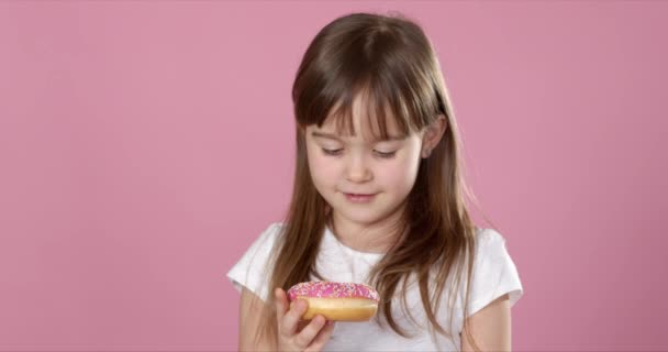 Studio ritratto di una bella bambina che tiene in mano una ciambella e profuma di sapore gustoso — Video Stock