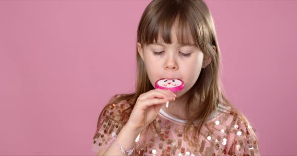 Jong vrolijk, glimlachend, mooi klein meisje met lief lolly snoep. Staande in lovertjes jurk — Stockvideo