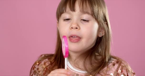 Rozkošná mladá dívka pózuje s růžovým lízátkem sladkosti. Usmívat se do kamery se vší radostí — Stock video