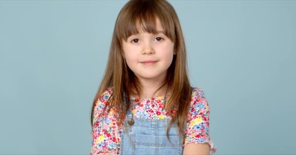 Douce petite fille de 6-7 ans posant en jean dungarees et chemisier motif fleur sur bleu — Video