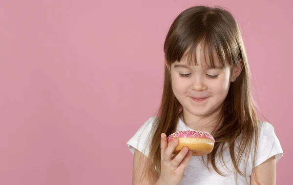一个漂亮的小女孩拿着一个甜甜圈，闻起来味道鲜美的工作室肖像 — 图库照片