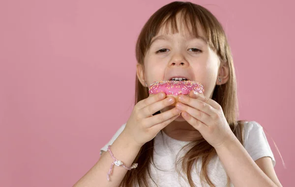 Bonito jovem caucasiano menina pego comer um doce rosa donut — Fotografia de Stock