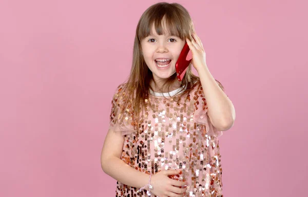 Alegre niña rubia de 6-7 años en vestido de lentejuelas hablando en el teléfono móvil . —  Fotos de Stock