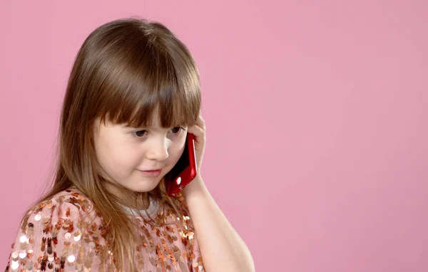 Glada lilla blonda liten flicka 6-7 år gammal i paljettklänning talar på mobiltelefon. — Stockfoto