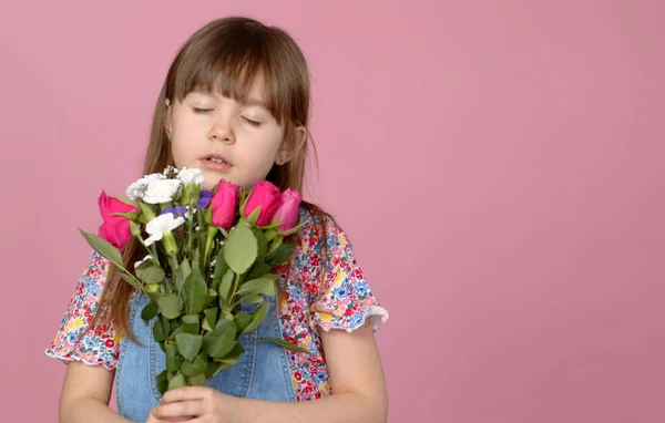 Linda niña sonriente adorable sosteniendo ramo de flores de primavera aisladas sobre fondo rosa —  Fotos de Stock