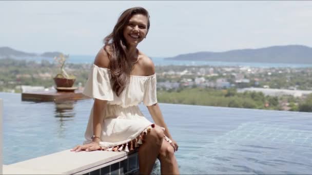 Feliz mujer relajada sentada junto a la piscina contra la costa del océano — Vídeo de stock