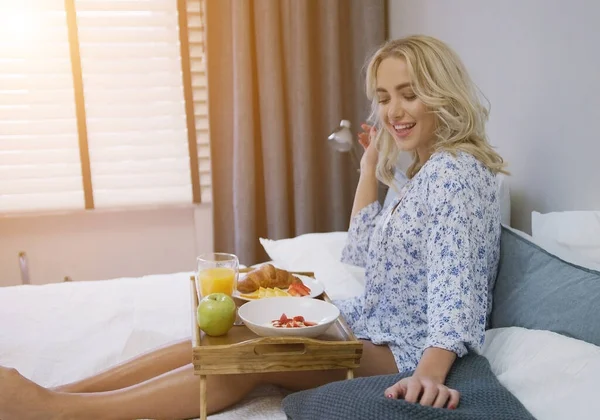 Atractiva joven con camisa desayunando sentada en la cama con bandeja —  Fotos de Stock