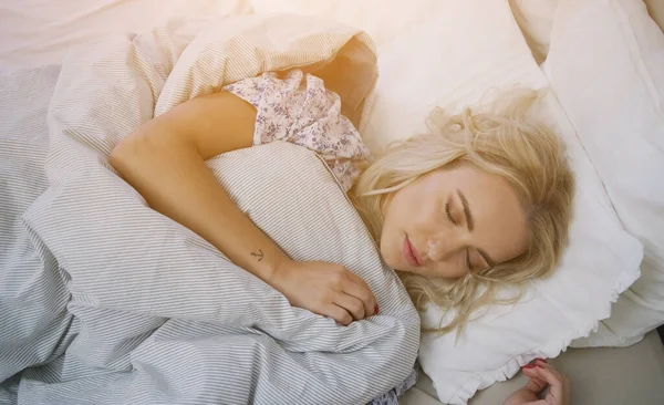 Underbar ung kvinna med blont hår liggande i bekväm säng under varm filt — Stockfoto