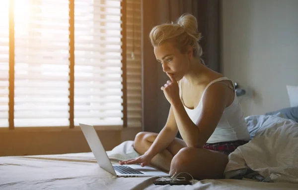 Schöne junge Frau im Schlafanzug sitzt auf dem Bett mit Laptop — Stockfoto