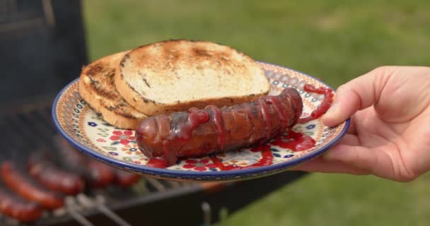 Женщина держит красочную керамическую тарелку с колбасой барбекю и хлебом на гриле . — стоковое видео