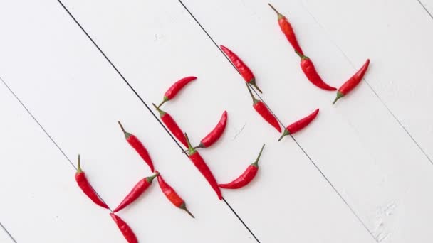 Slovo HELL vytvořené s malými červenými papričkami. Umístěno na bílém dřevěném stole — Stock video