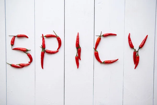 Uma palavra SPICY formada com pequenas pimentas vermelhas. Colocado em mesa de madeira branca — Fotografia de Stock