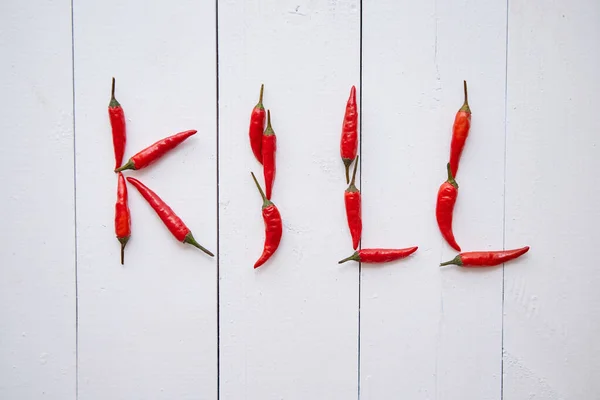 Uma palavra KILL formada com pequenas pimentas vermelhas. Colocado em mesa de madeira branca — Fotografia de Stock