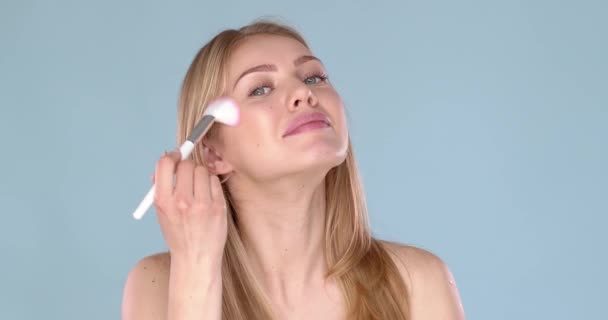 Hermosa mujer rubia aplicando polvo de maquillaje en su cara usando cepillo — Vídeos de Stock