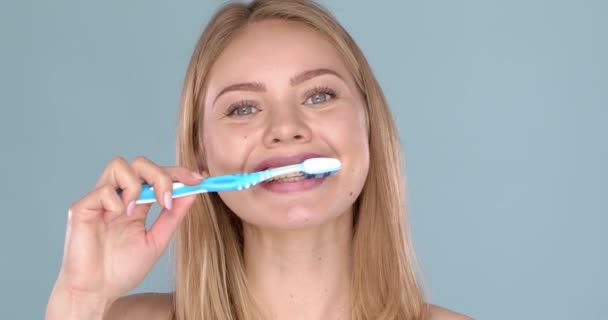 Mujer con sonrisa adorable cepillándose los dientes, aislada sobre fondo azul — Vídeo de stock