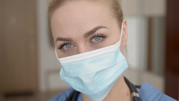 Retrato de una joven doctora en máscara médica, abrigo azul y estetoscopio — Vídeos de Stock